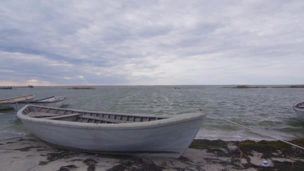 A wooden fishing boat moored on a sandy and grassy shore at sunset with a cloudy sky, time lapse. — Vídeos de Stock