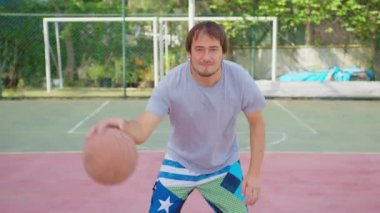 Spor sahasında duran ve elinde basketbol topu tutan bir adam..