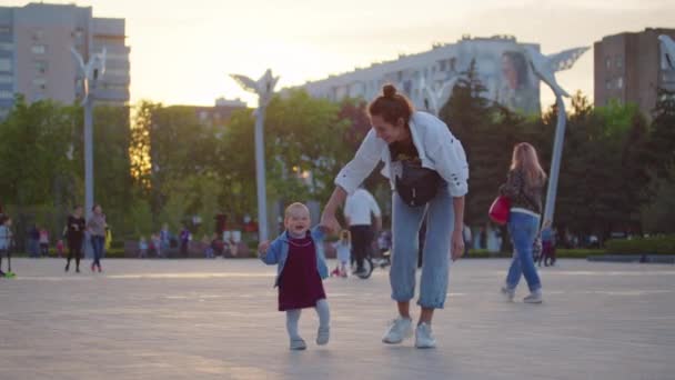 Bebek yürümeyi öğreniyor, yürümeyi öğreniyor. Annesiyle ilk adımlarını atıyor. Çocuğa dışarıda öğretmenlik yapıyor.. — Stok video