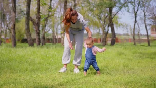 Baby första steget utomhus promenader. mor hjälpa sitt barn att gå sitt första steg i parken. — Stockvideo