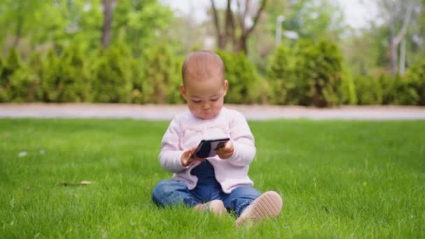 Baby Mädchen konzentriert sich auf ihr Handy im Park. Babys und Technologie. — Stockvideo