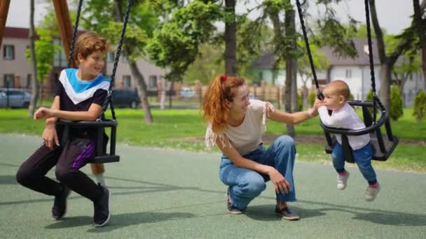 Lycklig familj mamma med barn rullar det lilla barnet i flykt på swing i parken. På helgerna går mor och dotter. Familjepromenader i parken. Ung och ung förälder. begreppet barn och familj. — Stockvideo
