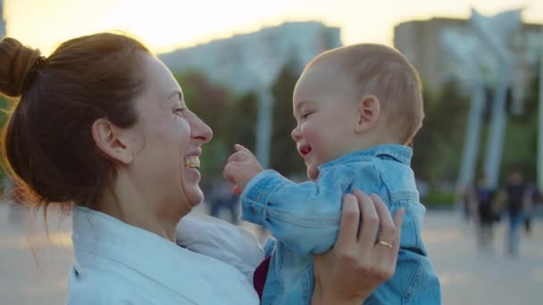 Glücklich lächelnde Mutter hält ihr Kleinkind in den Armen und hat Spaß sie lachen. Nahaufnahme. — Stockvideo