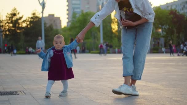 Bebé aprendiendo a caminar niño pequeño dando los primeros pasos con la madre ayudando al niño a enseñar al aire libre. — Vídeo de stock