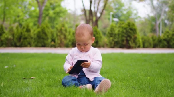 Baby Mädchen konzentriert sich auf ihr Handy im Park. Babys und Technologie. — Stockvideo