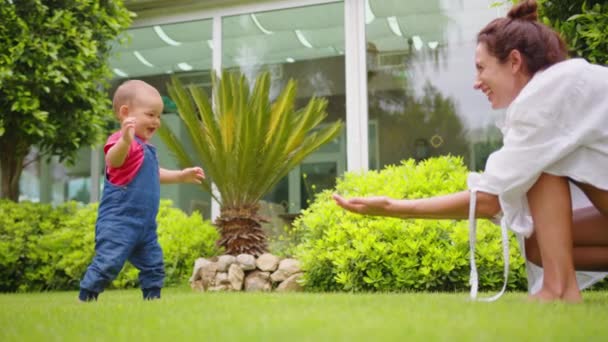 Мала дитина вчиться ходити. Мати вчить дитину робити перші кроки на зеленій траві влітку.. — стокове відео