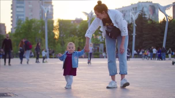 Baby första steget utomhus promenader. mor hjälpa sitt barn att gå sitt första steg i parken. — Stockvideo