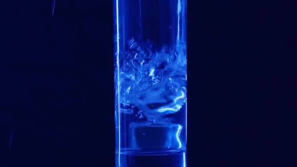 Wlewanie wody mineralnej do szklanki z kostkami lodu na czarnym tle zbliżenie z rozpryskami i kroplami. Zwolniony ruch. — Wideo stockowe