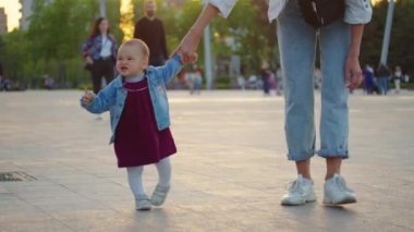 Küçük bebek yürümeyi öğreniyor. İlk Basamaklar. Ebeveynler çocuklarına yaz aylarında yeşil çimlerde ilk adımları atmayı öğretiyor. Mutlu çocukluk ve ebeveynlik kavramları. Aile sevgisi.