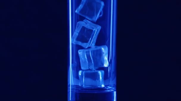 Häll mineralvatten i ett glas med isbitar på en svart bakgrund närbild med stänk och droppar. Långsamma rörelser. — Stockvideo