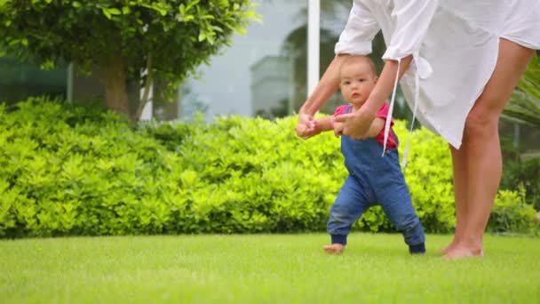 Bedårande ett år gammal flicka gör sina första steg utomhus. Slow Motion Video från de första stegen av Kid. Solig dag och grönt gräs. — Stockvideo