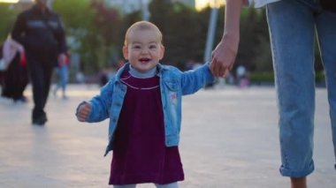 Küçük bebek yürümeyi öğreniyor. İlk Basamaklar. Ebeveynler çocuklarına yaz aylarında yeşil çimlerde ilk adımları atmayı öğretiyor. Mutlu çocukluk ve ebeveynlik kavramları. Aile sevgisi.