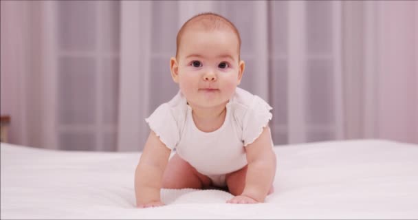 Härlig baby leker hemma i sovrummet tittar på kameran leende 9 månader glad baby spelar. Underbar liten flicka krypa i sängen liten flicka porträtt. — Stockvideo