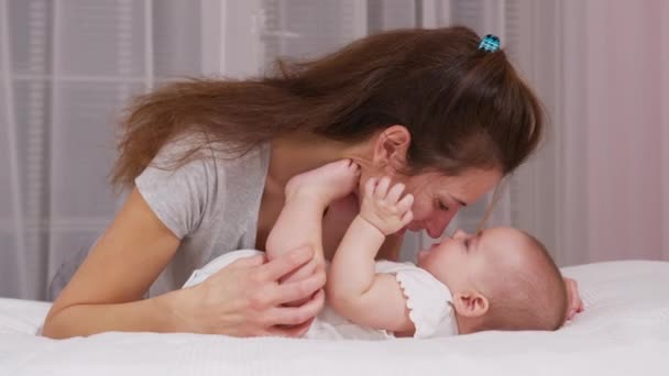 Gyengéd szerető fiatal anya csókolózik aranyos kis baba lány lánya fekszik az ágyban. Boldog gondoskodó anya és vicces imádnivaló csecsemő gyermek fia játszik szórakozás a hálószobában. — Stock videók