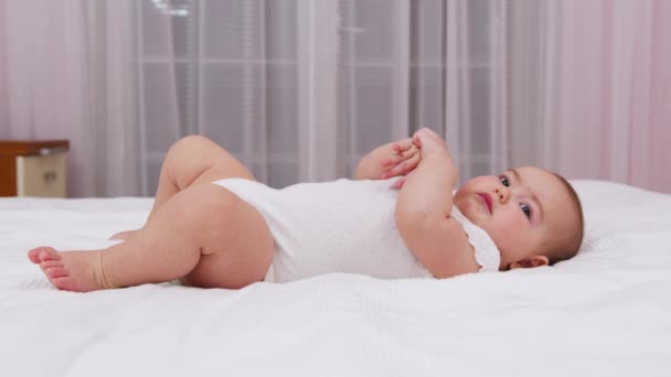 Frumos zâmbitor copil: un bebeluș superb se află pe pat . — Videoclip de stoc
