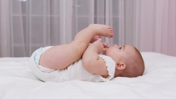 Hermoso bebé sonriente: Un bebé pequeño y hermoso yace en la cama. — Vídeo de stock