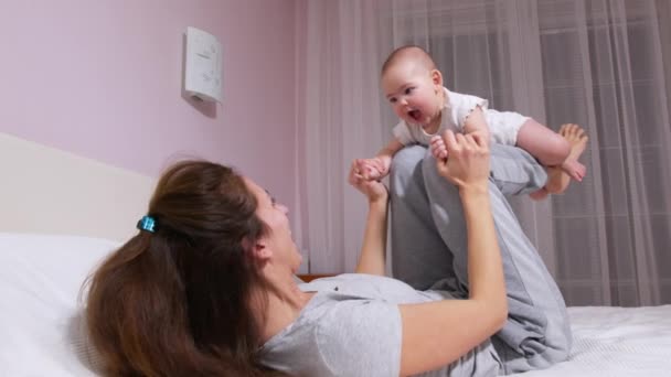 Selamat malam ibu muda yang sehat mengangkat bayi perempuan lucu sampai dengan bermain pesawat di tempat tidur. Loving mom doing yoga gymnastic exercise with funny adorable baby in cozy bedroom. — Stok Video