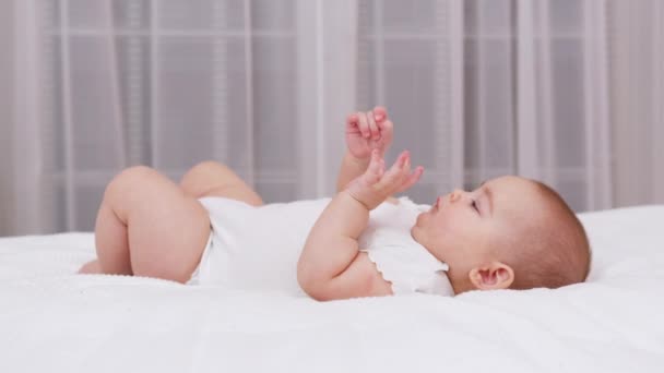 Hermoso bebé sonriente: Un bebé pequeño y hermoso yace en la cama. — Vídeo de stock