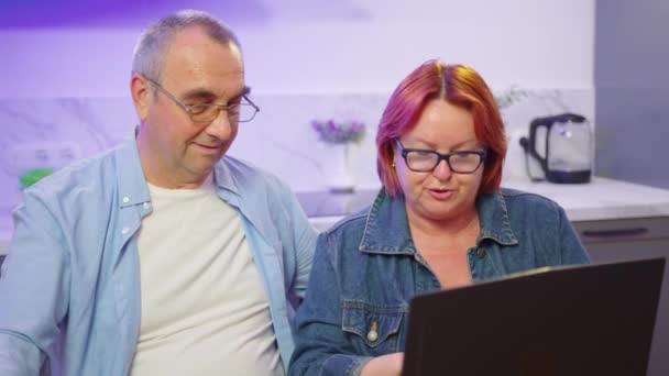 快乐的中年夫妇使用笔记本电脑一起上网购物，年长的退休家庭阅读讨论网络计算机新闻，选择在家里的网站上旅行. — 图库视频影像