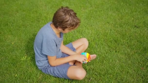 緑の自然を背景にポピットで遊ぶ子供の手のクローズアップ。子供はポパイを演じる。シリコーン抗ストレス感覚おもちゃ。トレンド2021 。ポップそれはカラフルなシンプルディンプル再利用可能なストレスリリーフおもちゃです. — ストック動画