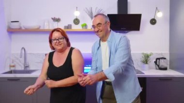 Mutlu yaşlı çift mutfakta gülüyor, güzel orta yaşlı büyük anne ve büyük baba evde birlikte eğleniyor yıldönümünü kutluyorlar sevgi şefkatinin tadını çıkarıyorlar..
