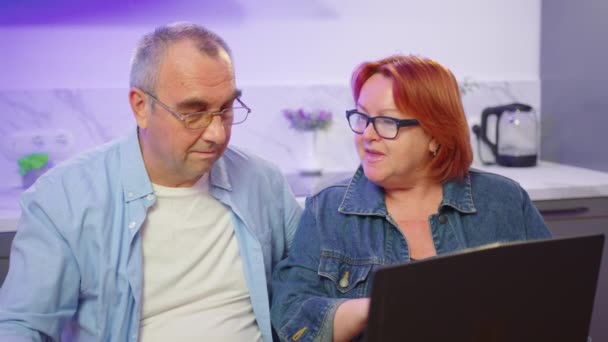 Feliz velho casal de meia-idade usando laptop conversando juntos fazendo compras on-line, sênior maduro aposentado leitura da família discutir internet notícias do computador. — Vídeo de Stock