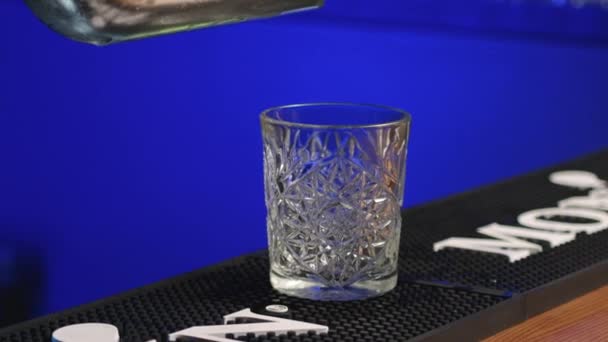 Auténtico camarero profesional creando una bebida de cóctel. Barman experimentado vertiendo bebidas alcohólicas en vidrio antes de servir - concepto de comida y bebida de cerca, luz de fondo azul. — Vídeo de stock