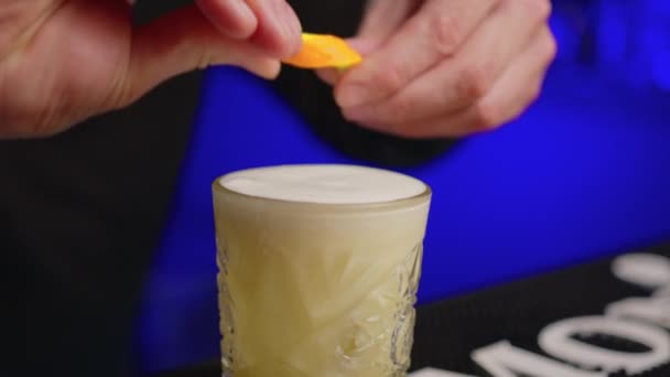 Camarero exprime cáscara de naranja en un vaso con un cóctel, luego pone el resto en el vaso de cerca. Cantinero haciendo cóctel alcohólico en bar moderno. — Vídeos de Stock