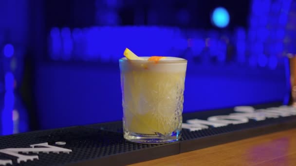 Barman serre la croûte orange dans un verre avec un cocktail, puis met le reste dans le verre fermer. Bar faisant cocktail alcoolisé dans un bar moderne. — Video