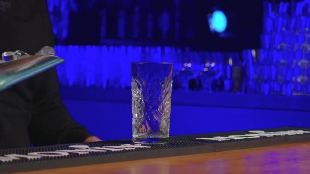 Αυθεντικός επαγγελματίας μπάρμαν δημιουργεί ένα κοκτέιλ ποτό. Έμπειρος μπάρμαν ρίχνει αλκοολούχο ποτό στο ποτήρι πριν από το σερβίρισμα - τροφίμων και ποτών έννοια κοντά, μπλε πίσω φως. — Αρχείο Βίντεο