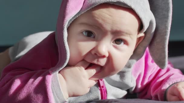 Retrato de um bebê recém-nascido agradável, deitado em seu estômago em uma cama branca chupando os dedos, olhando curiosamente para a câmera com a boca aberta. — Vídeo de Stock