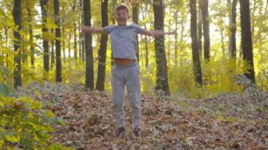 Genç bir çocuk ormanda sonbahar yapraklarıyla kıvrılıp onları fırlatıyor..