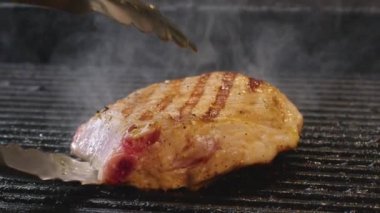 Kızarmış etli biftek, baharat ve otlarla birlikte, yanan kömürlerin içinde, bbq ızgarası, alevler ve duman. Izgara çizgili sulu biftek piknik kutlaması için hazır. Barbekü ızgarası.