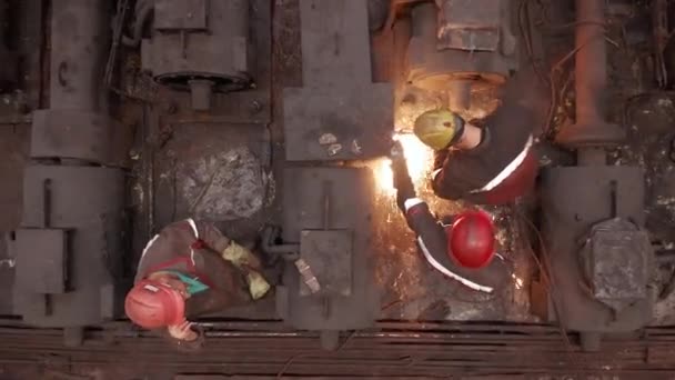 Vista superior. Un trabajador de pie y el procesamiento de una estructura de metal con chispas brillantes en la planta de fabricación de coches de ferrocarril. Trabajo duro. Vista trasera. Dentro de una instalación industrial. Taller industrial. — Vídeos de Stock