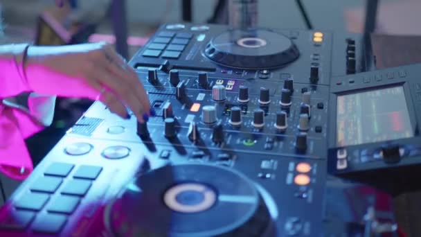 De cerca. Consola de control de sonido DJ para mezclar música dance en discoteca. Manos tocando botones deslizadores, tocando música electrónica en la cubierta de mezcla, iluminación de color en la fiesta de baile de discoteca. — Vídeo de stock