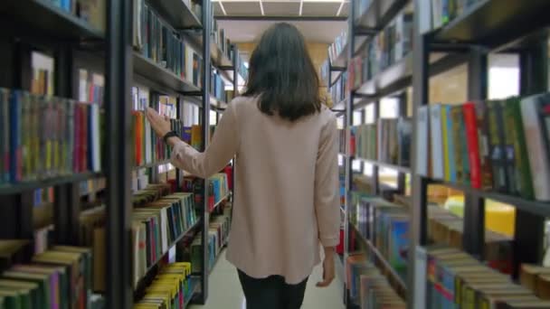 Bakspeilet av en tenåringsjente med ryggsekk på skolebiblioteket. Tenåringer som går mellom hyller i bokhandelen. Utdanning, elevlivsstil og læringsbegrep. – stockvideo