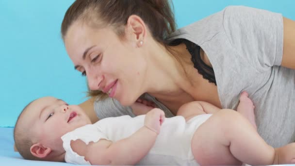 Teder liefdevolle moeder zoenen bonding met schattig klein meisje dochter liggend op bed. gelukkig zorgzame mam en grappig schattig baby kind zoon spelen plezier in slaapkamer. — Stockvideo