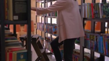 Genç bir kız kitap almak için merdivenleri çıkıyor. Bu video eski ahşap kütüphane merdivenlerini ve güzel bir kitap kütüphanesini gösteriyor..