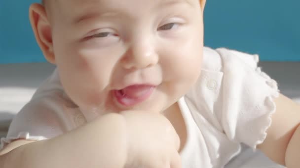 Krásné usměvavé dítě: Nádherné malé dítě leží na posteli a usmívá se na kameru s pěkným měkkým ostřením pozadí. — Stock video