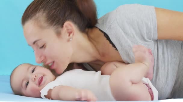 Tender kärleksfull mamma kysser bindning med söt liten flicka dotter liggande på sängen. Glad omtänksam mamma och rolig bedårande spädbarn son leka ha kul i sovrummet. — Stockvideo