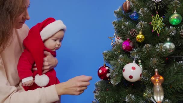 Anne bebeğiyle Noel ağacının yanında. Anne ve bebek yeni yıl ağacı ile oynuyorlar.. — Stok video