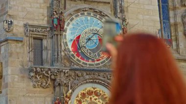 Prag Astronomik Saati, ortaçağ astronomik saati, Prag, Çek Cumhuriyeti 'nin eski şehir meydanındaki eski belediye binasının duvarında bir kız cep telefonuyla fotoğraf çekiyor..
