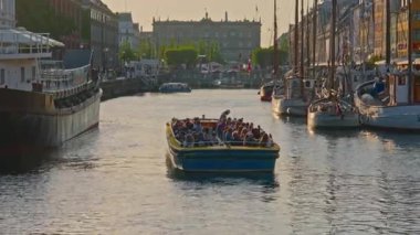 Kopenhag, Danimarka - 21.08.2025: Tarihi Nyhavn rıhtım, kanal ve eğlence bölgesi. Gün batımında ünlü kanal boyunca turist taşıyan bir tekne yelken açar..