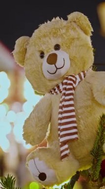 Oyuncak ayı süsü yakın plan. Noel ağacındaki oyuncak ayı süsü. Noel havası, Noel ağacı dışarıda süslenmiş oyuncaklar. Dikey video.