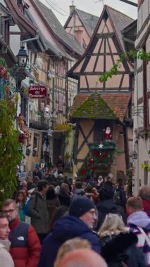 Eguisheim, Fransa - 3.12.2025: Noel için dekore edilmiş küçük, güzel bir köy. İnsanlar, Fransız köyü Eguisheim 'ın güzel dekore edilmiş sokaklarında geziniyor. Dikey video.