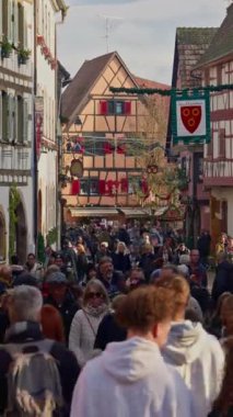 Eguisheim, Fransa - 3.12.2025: Noel için dekore edilmiş küçük, güzel bir köy. İnsanlar, Fransız köyü Eguisheim 'ın güzel dekore edilmiş sokaklarında geziniyor. Dikey video.
