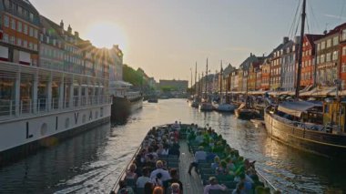 Kopenhag, Danimarka - 21.08.2025: Tarihi Nyhavn rıhtım, kanal ve eğlence bölgesi. Gün batımında ünlü kanal boyunca turist taşıyan bir tekne yelken açar..