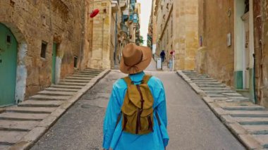 Şapkalı ve sırt çantalı bir kadın turist geleneksel eski caddelerde yürüyor ve Malta Valletta 'da onlara bakıyor..