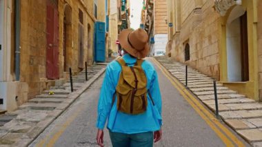 Şapkalı ve sırt çantalı bir kadın turist geleneksel eski caddelerde yürüyor ve Malta Valletta 'da onlara bakıyor..