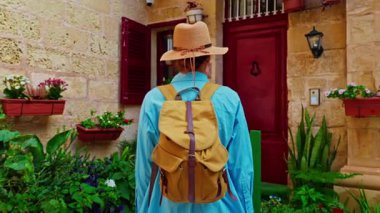 Şapkalı ve sırt çantalı bir kadın turist Mdina, Malta 'daki geleneksel dar sokaklar boyunca yürüyor..